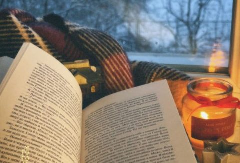 Cozy winter reading scene with an open book, journal, and candle by a window, creating a calm space for reflection and emotional wellness.
