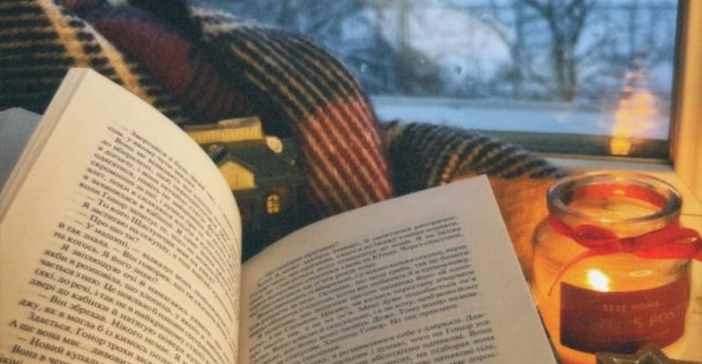Cozy winter reading scene with an open book, journal, and candle by a window, creating a calm space for reflection and emotional wellness.