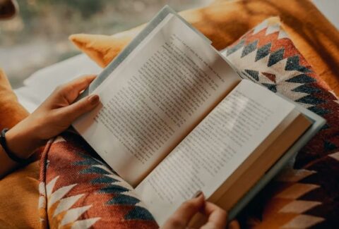 A person holding an open book while reading under a warm blanket, symbolizing reflection, emotional wellbeing, and the healing power of reading.