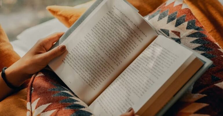 A person holding an open book while reading under a warm blanket, symbolizing reflection, emotional wellbeing, and the healing power of reading.