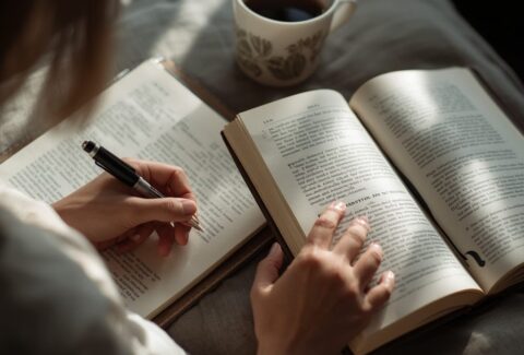 A person writing in a journal beside an open book, symbolizing reflection, courage, and the power of finding one's voice through reading.
