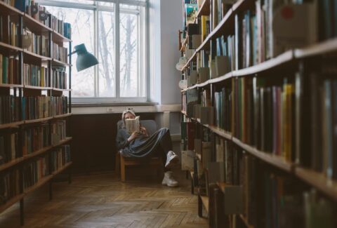 Woman reading a book in a quiet library, reflecting on stories, identity, and personal perspective