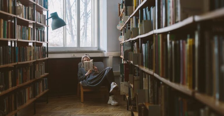Woman reading a book in a quiet library, reflecting on stories, identity, and personal perspective