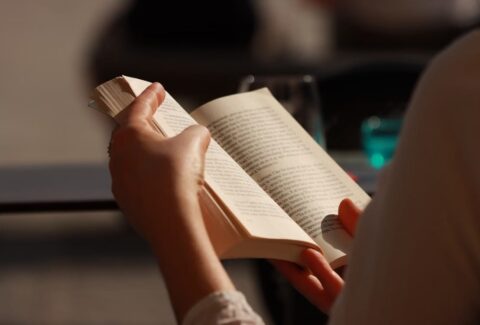 Woman reading a book beside a window, reflecting the themes of self-discovery, personal reflection, and new possibilities