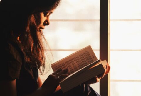 Woman reading a book beside a window in a quiet moment of reflection