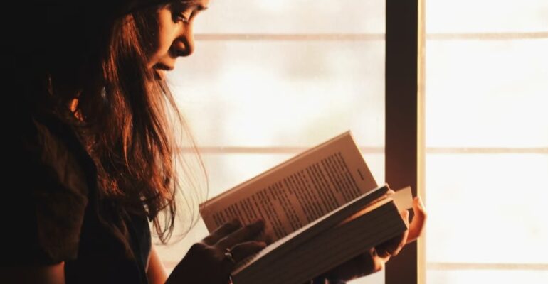 Woman reading a book beside a window in a quiet moment of reflection