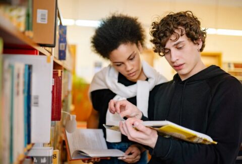 Two people reading books together in a library